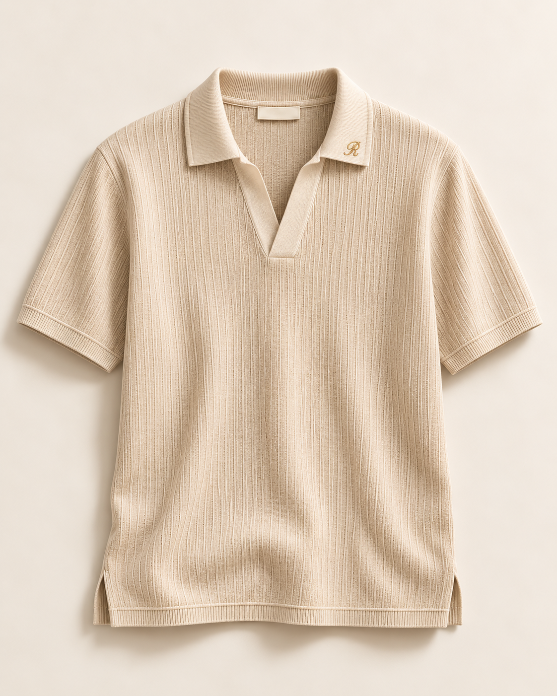 Corner (E05), polo beige a collo aperto con ricamo R; capo intero. Il bordeaux resta una direzione progettuale.